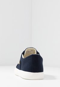 Námořnické plátěné tenisky s texturovaným svrškem, bílou gumovou podrážkou a malým zlatým akcentem na boku. Zadní pohled ukazuje design a tvar.