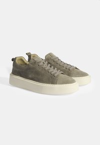 Gray suede sneakers with a rounded toe, flat cream sole, and matching laces. Features a rear pull tab and textured side panels.