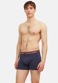 Marinefarbene Boxershorts mit einem burgunderfarbenen Gummibund, der mit dem „JACK & JONES“-Logo versehen ist. Hergestellt aus weichem Stoff, passgenau geschnitten. Glatte Textur.