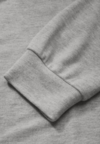 Close-up van de mouwboord van een lichtgrijze sweatshirt, waarbij de zachte gebreide stof en het geribbelde boorddetail zichtbaar zijn.