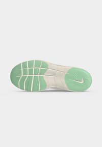 Σόλα παπουτσιού Nike με ανοιχτό πράσινες λαστιχένιες περιοχές πρόσφυσης και λευκές αυλακώσεις σε μπεζ βάση, που δείχνει το λογότυπο Nike swoosh.