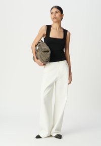 Top sin mangas de escote cuadrado negro, pantalones blancos de pierna ancha y zapatos negros de punta; sosteniendo un bolso marrón de textura tejida. Diseño simple, colores neutros.