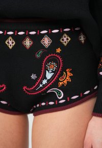 Melni auduma šorti ar krāsainu paisley un ziedu izšuvumu. Jostasvieta rotāta ar dekoratīvām šuvēm rozā un bordo krāsā.