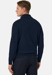 Pull en maille bleu marine avec un col montant, design ajusté et ourlet côtelé. Texture douce, look superposé et délicats détails de couture.