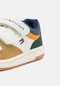 Sneakers i vit läder och brun mocka med blå, grön och orangea detaljer. Kardborreband och logotyp på sidan. Gummisula.