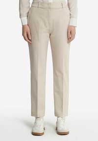 Jasno beżowe, dopasowane spodnie o prostym kroju, wykonane z gładkiego materiału, z paskami na pasek i kieszeniami po bokach. W zestawie z białymi trampkami.