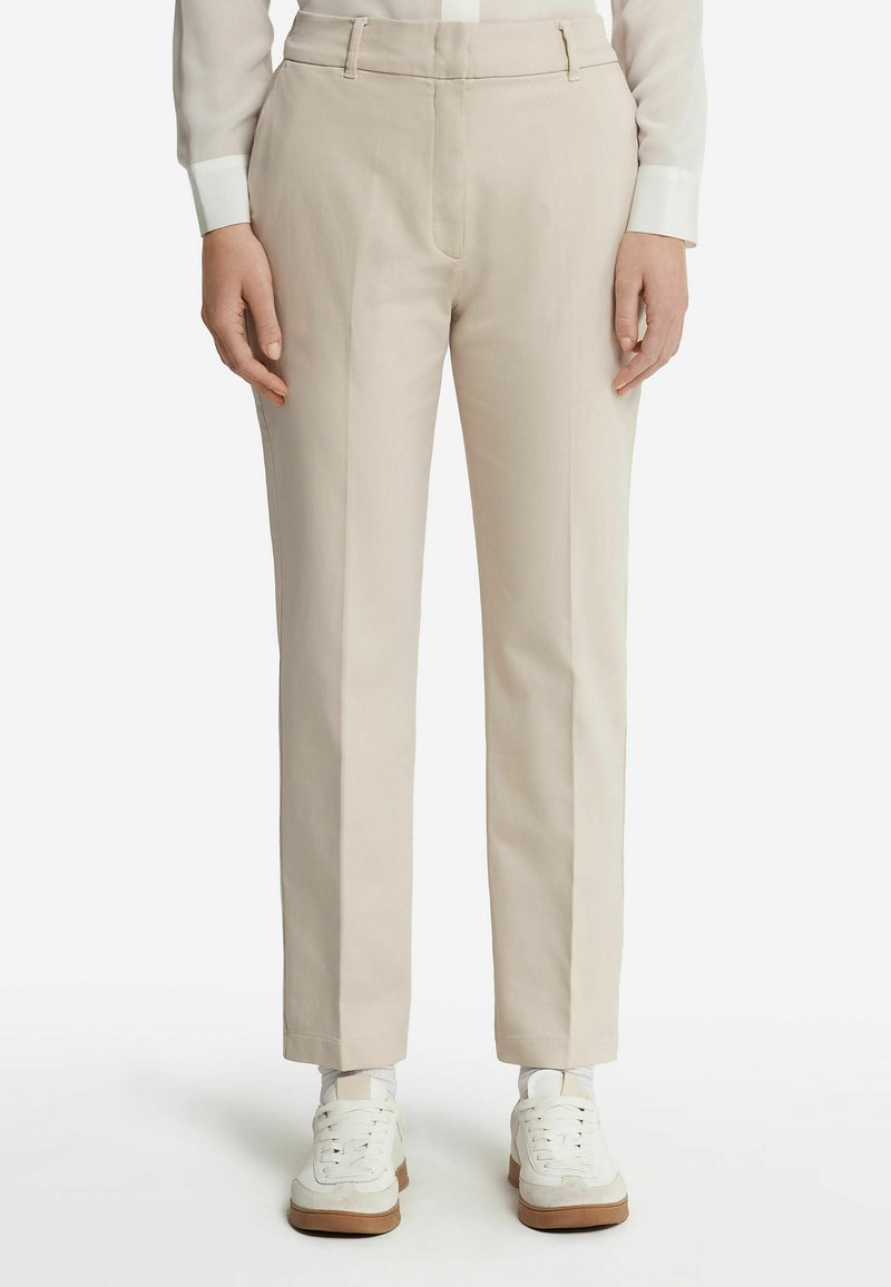 Jasno beżowe, dopasowane spodnie o prostym kroju, wykonane z gładkiego materiału, z paskami na pasek i kieszeniami po bokach. W zestawie z białymi trampkami.
