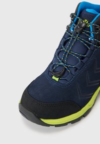 Bota de senderismo azul marino con un upper de ante texturizado, punta de goma negra y acentos en verde neón. Cuenta con un sistema de cordones de ajuste rápido y detalles con patrón.