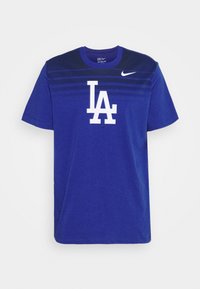 Camiseta de algodón azul con cuello redondo, mangas cortas y un gráfico blanco de "LA" en la parte frontal. Rayas horizontales en un azul más oscuro cerca de los hombros.