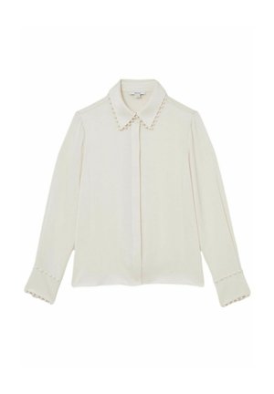 Balta blūze ar norādītu apkakli, pērļu akcenti apkaklē un aprocēs, garām piedurknēm un taisnu griezumu. Gluda auduma tekstūra.