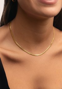 Collar de oro con un diseño liso y plano que descansa sobre la piel, con un acabado sutilmente texturizado y una ligera curva a lo largo del escote.