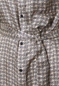 Beige fabric dress with a repeating black “PINKO” pattern, featuring a tied waist, button closure, and subtle textured finish.