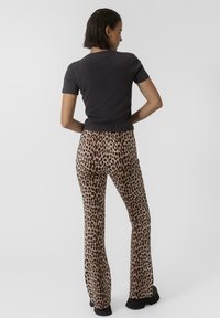Svart figurnära kortärmad skjorta kombinerad med beige utsvängda byxor med ett svart leopardmönster. Texturerad tyg och enfärgade svarta skor.