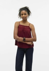 Bordeaux cami met kantdetails, dunne straps en een losse pasvorm, gecombineerd met donkere jeans. Gladde textuur met een vloeiende uitstraling.