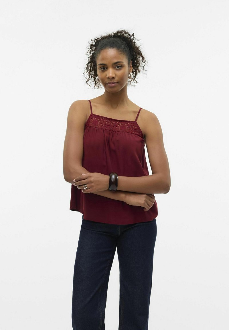 Bordeaux cami met kantdetails, dunne straps en een losse pasvorm, gecombineerd met donkere jeans. Gladde textuur met een vloeiende uitstraling.