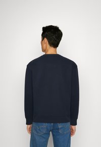 Sudadera navy con cuello redondo, corte relajado y mangas largas, hecha de tejido suave. Mostrada desde atrás, combinada con jeans de color azul claro.