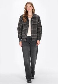 Rutig jacka i grå, röd och svart ullblandning, med tryckknappar och ribbade ärmar. Buren över en ljusfärgad topp och svarta jeans.