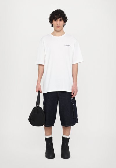 T-shirt en coton blanc à manches courtes, associé à un short cargo en denim foncé avec des poches latérales. Sac noir et bottes noires épaisses.