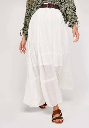 Gonna maxi bianca realizzata in tessuto leggero, con un design a strati e un pannello trasparente. Abbinata a sandali marroni per un contrasto.