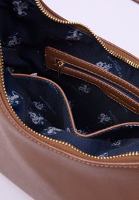 Interno di una borsa sintetica marrone con un rivestimento in tessuto blu scuro caratterizzato da un motivo chiaro ripetuto. Include una tasca con zip e una cerniera dorata.