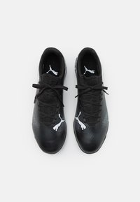 Zapatillas deportivas negras con una superficie texturizada, que cuentan con cordones negros y logotipos blancos de Puma a cada lado. Diseño moderno y elegante con un ajuste ceñido.