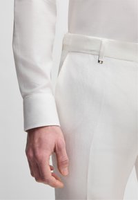 Vit linnekostym med texturerad yta, som har en slim fit-design, skräddarsydda ärmslut och ett matchande bälte för en enhetlig look.