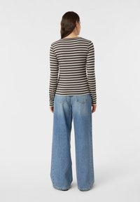 Brązowo-kremowa bluzka w paski z długim rękawem, zestawiona z szerokimi, jasnobłękitnymi jeansami o standardowych kieszeniach i luźnym kroju.