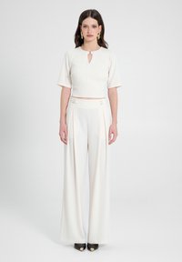 Top bianco corto con dettagli a chiave e maniche corte, abbinato a pantaloni a gamba larga a vita alta con cintura con accenti metallici.