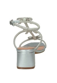 Sandali con tacco argento, dotati di sottili cinturini incrociati e una finitura texturizzata e lucida. Presentano un tacco a blocco e un dettaglio a fiocco sul retro.