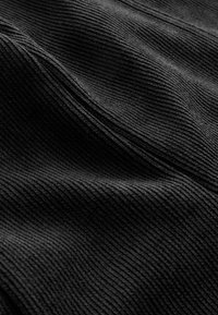 Gros plan sur un tissu velours côtelé noir montrant des côtes parallèles surélevées et une texture douce avec lumière et ombre sur les plis.
