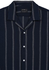 Camicia a maniche corte relaxed fit blu navy con strisce verticali bianche, tessuto testurizzato, colletto e quattro bottoni bianchi sul davanti.