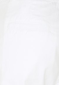 Tela blanca con una textura suave y un único bolsillo trasero. La costura es visible a lo largo de los bordes, manteniendo un diseño minimalista.