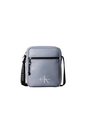 Petit sac bandoulière gris clair Calvin Klein avec poche avant zippée, logo embossé et bandoulière noire réglable avec texte blanc.