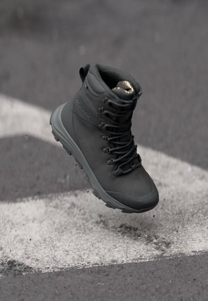 Botte en cuir noir avec une finition texturée, à lacets à l'avant et un soutien de la cheville. Dotée d'une semelle rembourrée et d'une semelle relief pour une meilleure traction.