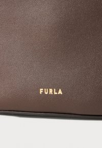 Texture en cuir brun avec le logo Furla embossé en or. Surface lisse et à grain fin. Aucun matériel ou accent supplémentaire visible.