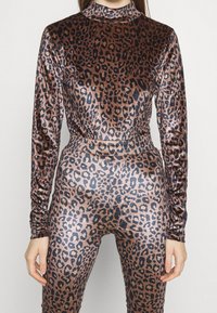 Outfit con stampa leopardata in tessuto lucido e elastico. Maniche lunghe, collo alto e design aderente. Schema colori: base marrone con macchie nere.