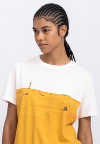 Korte mouwen T-shirt met een witte bovenkant en een gele onderzijde met een landschap ontwerp, inclusief heuvels en abstracte objecten.