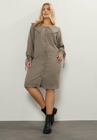 Brun- och beige rutig klänning med stor krage, knappar fram och långa ärmar; kombinerad med svarta ankelboots. Texturerat tyg.