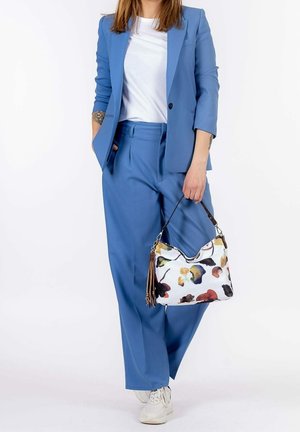 Light blue suit jacket and pants, white t-shirt, holding a white handbag with colorful abstract patterns and a brown strap. White sneakers.