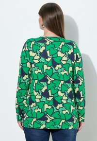 Grøn langærmet top med hjerteprint i forskellige nuancer og kontrasterende mørkeblå detaljer, vist bagfra.