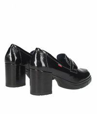 Zapatos de tacón de charol negro con un tacón grueso, que cuentan con una puntera redondeada y un detalle decorativo de correa en la parte delantera.