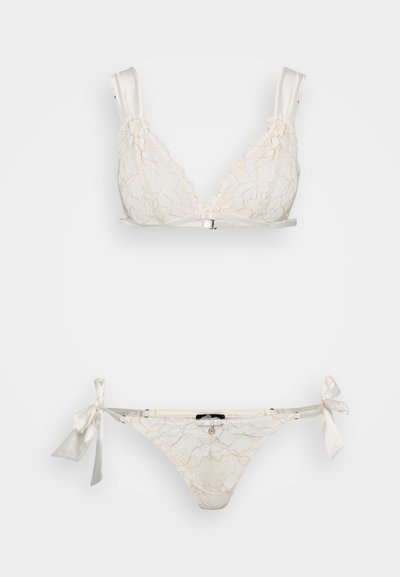 Brassière di pizzo cream con forma triangolare e spalline in satin, abbinata a slip bikini coordinati con lacci laterali e delicati motivi.