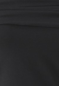 Svetlo čierna tkanina s preloženým švom blízko horného okraja, zobrazujúca textúru a mierne horizontálne preloženie.