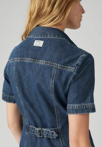 Jeansjurk met een aansluitende silhouet, korte mouwen, een taille met riem en een label aan de achterkant van de halslijn. Diepe blauwe kleur met een gestructureerde afwerking.