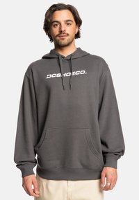 Gray hooded sweatshirt with a front pocket, featuring the white logo "DCSHOECO." on the chest. Made of a soft, textured fabric.