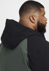 Chaqueta con capucha que presenta una capucha y mangas negras con un cuerpo verde, fabricada en un tejido suave, con costuras limpias y un diseño minimalista.