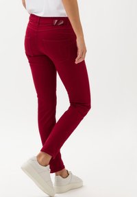 Jeans skinny carmesí con una cintura media, que cuentan con bolsillos traseros y costuras de refuerzo. Combinados con zapatillas blancas, que muestran una textura suave.