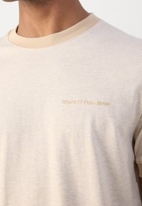 Camiseta de manga corta beige con un cuello redondo acanalado de un beige claro y un sutil logo de Marc O’Polo Denim bordado en el pecho en un tono a juego.