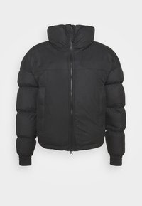 Svart pufferjacka med hög krage, framdragkedja och elastiska ärmmuddar. Har en quiltad textur och en kort silhuett.