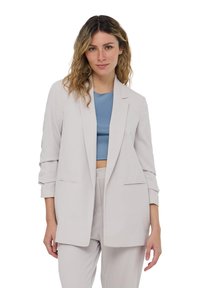 Blazer grigio chiaro con vestibilità su misura, dotato di chiusura a un bottone, rever a punta e due tasche frontali. Tessuto liscio con un design strutturato.